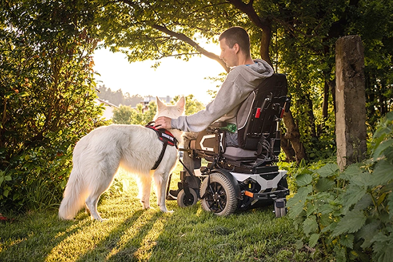 A man in an electric wheelchair powered by reliable VMAX deep-cycle mobility AGM batteries is relaxing with his dog.